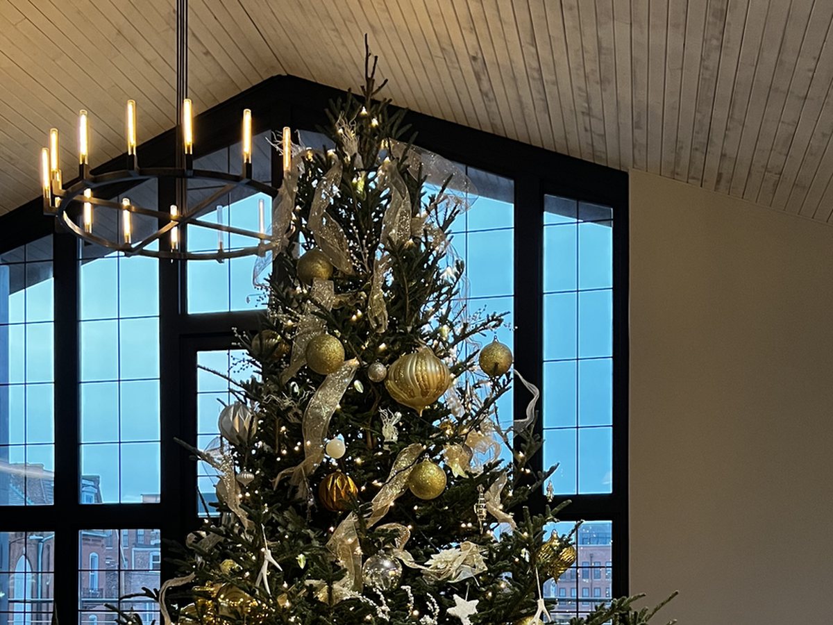 Gold-trimmed Christmas tree beneath the chandelier and gallery windows at THE 1301